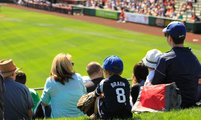 Kid sitting in a crowd at a baseball game with jersey and glove on.