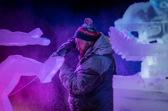 An ice sculptor using a power tool to carve a block of ice at the Freezefest ice battle