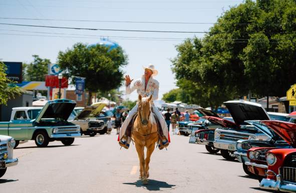 ChatGPT said:

A man dressed as Elvis in a rhinestone-studded white jumpsuit and cowboy hat rides a palomino horse down a street lined with classic cars at a Route 66 festival finale event in Amarillo.