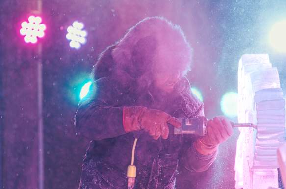An ice carver using a power tool to carve a sculpture during the Freezefest ice battle