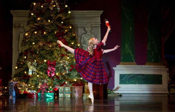 ballerina in a plaid dress posing in front of a Christmas tree