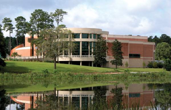 The Mobile Museum of Art building with curved architecture reflects in a serene pond, surrounded by lush green grass and trees.