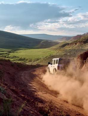 a dusty road with a vehcile driving along it through landscape