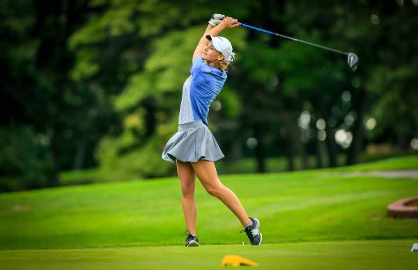 lady golfer in grey skirt and grey and royal blue shirt, white hat.full swing of club