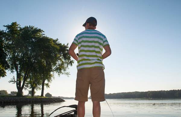 man standing on boat with tan shorts and green/white striped shirt fishing