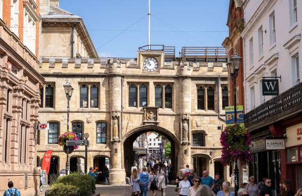 Lincoln Guildhall with people walking in the foreground and blue skies, with high street shops at the sides