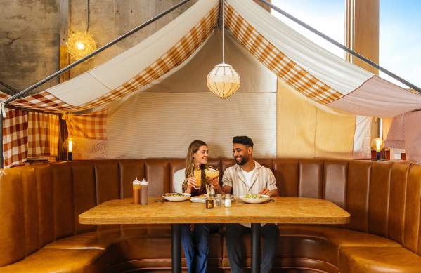 Young Couple sitting and holding drinks in a booth with a tent canopy overhead, at Union Rec