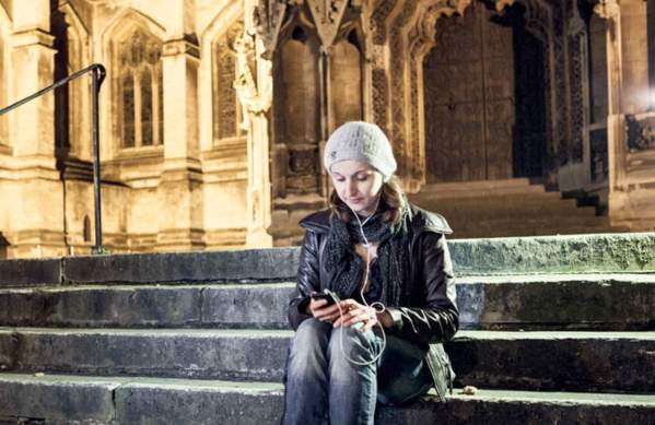 A woman sitting on the steps of St Mary Redcliffe Church wearing headphones listening to the Bristol audio tour