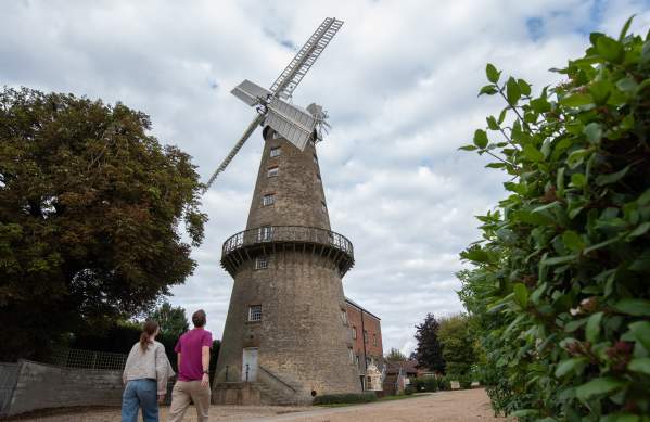 two people walking towards a windmill in the countryside