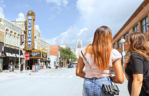 Two women looking down Liberty Street at the Michigan Theater and Bell Tower in the distant background with a mix of blue skies and white clouds.