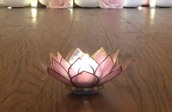 A wooden yoga studio floor has a lit candle and some decorative background pillows