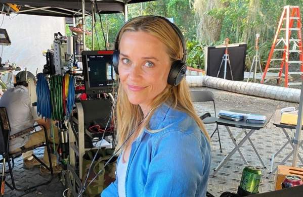 Reese Witherspoon on the film set of "Where the Crawdads Sing" wearing earphones with camera and sound equipment behind.