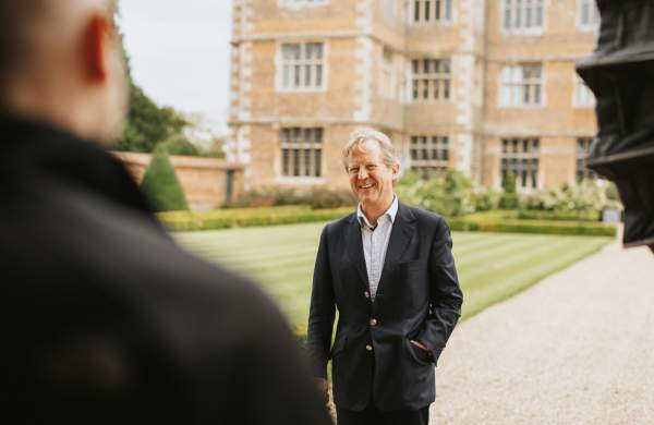 a man stood smiling on the grounds of a stately home with a camera crew in the foreground