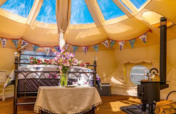 A glamping pod with woodburner and bed surrounded by flowers and bunting