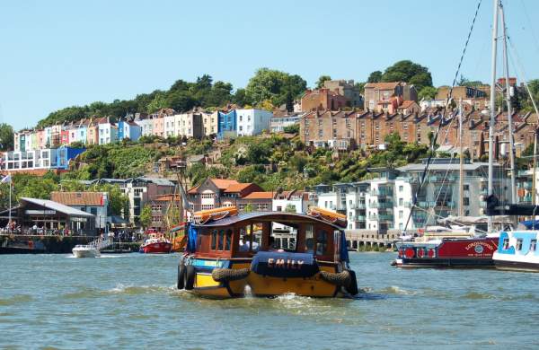 A Bristol Ferry Boat sailing eastwards on Bristol's Harbourside, with the SS Great Britain and colourful houses of Cliftonwood in the background - credit Visit West