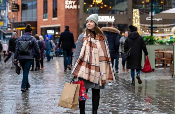 A woman in a scarf is stood in the centre of the Cornhill Quarter in Lincoln, holding shopping bags.