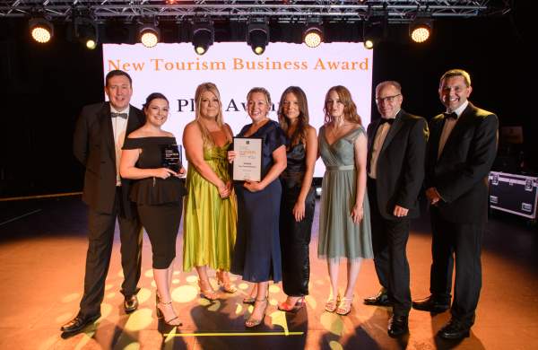 people stood on a stage in front of an awards screen in black-tie attire with an award in hand