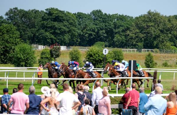 jokeys on horses racing with spectators in foreground
