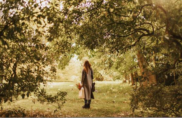 A woman surrounded by trees, looks up at the autumn leaves