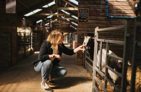A woman knelt down petting a goat in an indoor farm barn