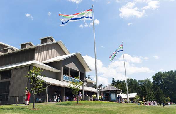 A theater building with a blue sky above, green grass and flags waving above it.