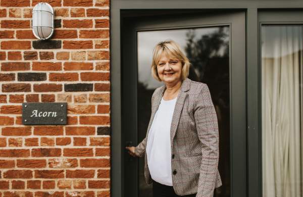 A woman holding the door open of a holiday cottage