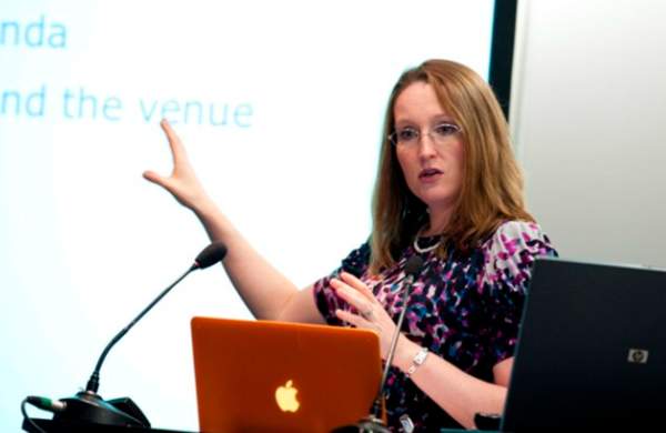 a woman stood in front of a presentation screen pointing at the slides