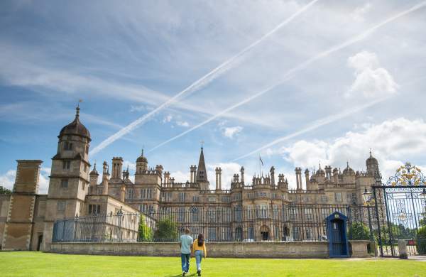 A sunny day exterior of Burghley House near Stamford with two people walking towards the gates