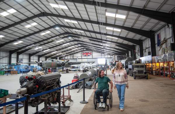 two people in a hanger with aviation props and planes in background