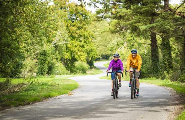 Two people cycling through a forest on a path