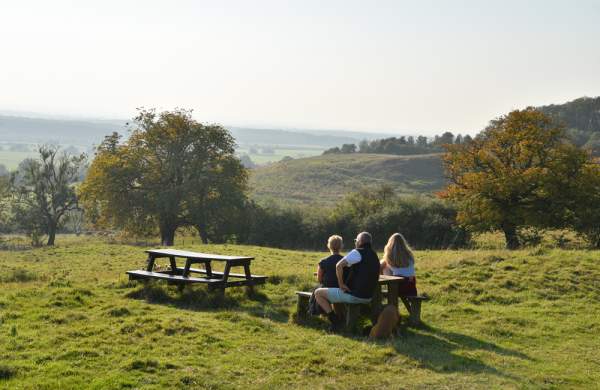 A group of people sitting on a bench in Tealby, Lincolnshire Wolds, looking out at a picturesque view of the trees and landscape.
