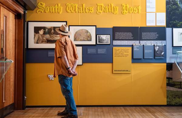 A man looking at picture in an exhibition on a yellow wall.
