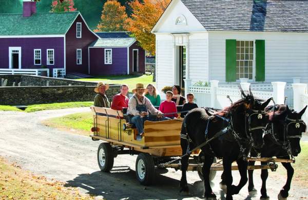 an image of a horse drawn carriage carrying people in front of historic houses with fall leaves behind it
