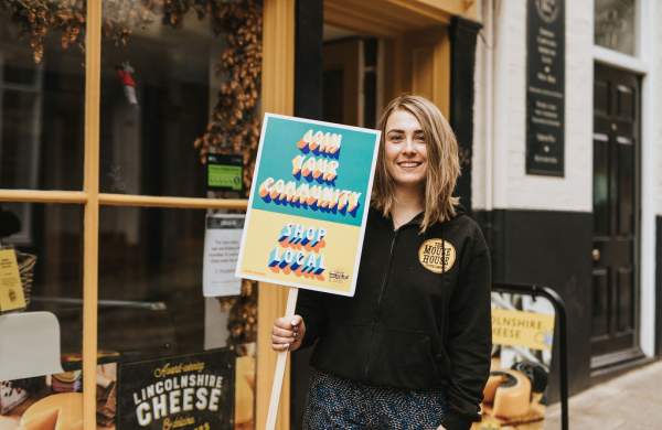 A woman holding a sign outside of a shop that reads 'shop local'