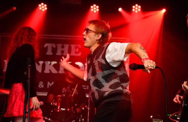 A male singer on a stage wearing sunglasses, holding a microphone, dancing