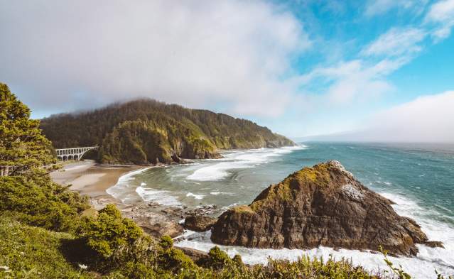 Viewpoint from Heceta Head Lighthouse showing rocky coastline and a large bridge.