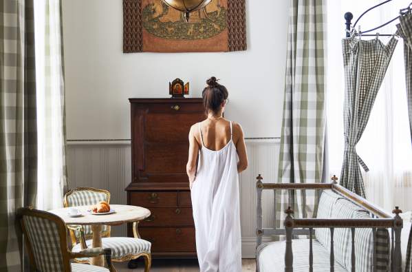 A woman in a white dress moves through a guest room at the upscale New Orleans boutique hotel Hotel Peter and Paul in the Marigny.