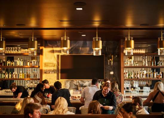 Warm lights glow over a bustling dining room with servers and diners.