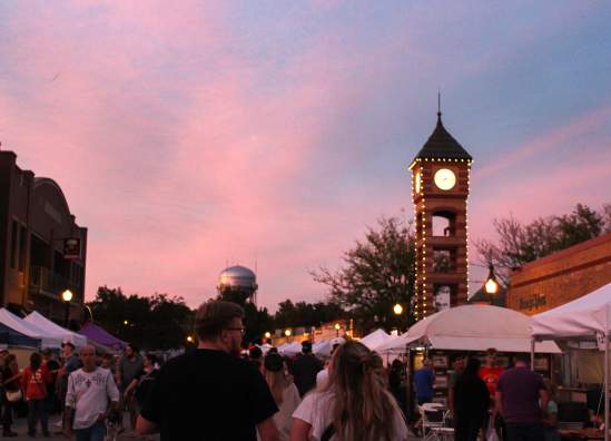 Couple walks through the streets of Downtown Overland Park as a blue, purple and pink sunset is cast over the Clock Tower.
