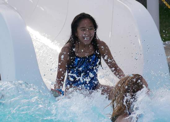 A smiling girl with dark hair splashed into the pool at the end of a waterslide.