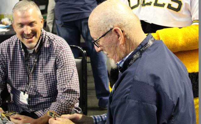 Salt Lake Bees Mascot standing behind two men sitting at a table talking