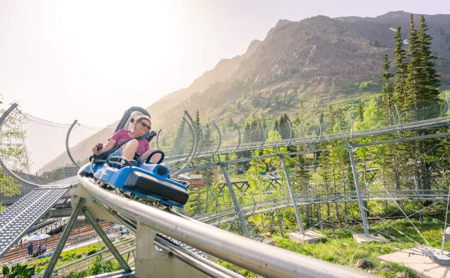 Woman looking like she is going fast around a corner on a single person coaster with sky and mountains around her