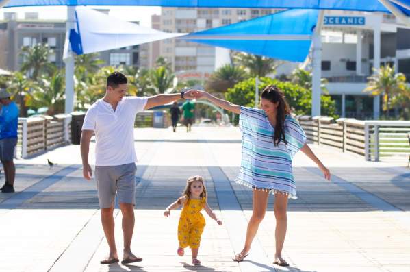 a dad and mom making a hand bridge over their young daughter as they walk on the Pompano Beach Pier