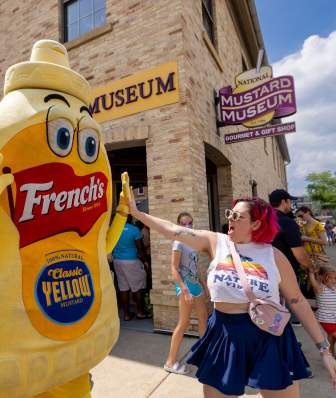 A white woman high fives a person wearing a mustard costume outside the National Mustard Museum in Middleton