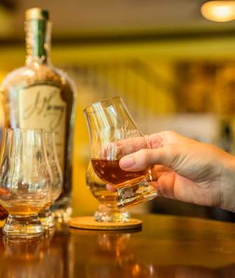 A person holds a small glass of bourbon as part of a bourbon flight at J. Henry and Sons Distillery