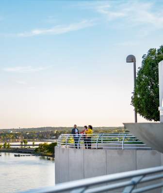 A wide view of three people enjoying drinks on the rooftop of Monona Terrace with Lake Monona and the sunset in the background