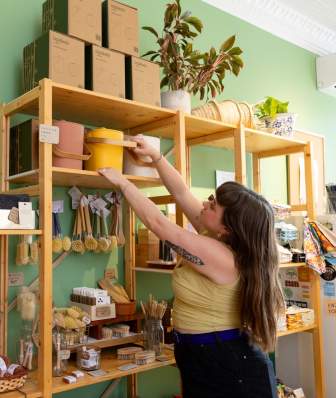 A woman grabs a small compost bin from a shelf at Green Life Trading Co.