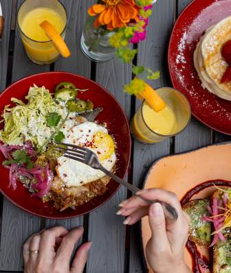 An overhead view of a table full of bright colored plates with various breakfast dishes and glasses of orange juice being served.