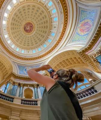 A white woman uses her phone to take a picture of the rotunda ceiling inside the Wisconsin State Capitol