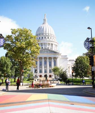 A wide shot of the Wisconsin State Capitol building from State Street with a view of the rainbow pride crosswalk
